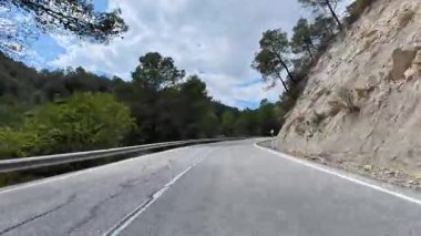 Kıvrımlı, kıvrımlı bir dağ yolunun nefes kesici manzarası, bereketli ağaçlar ve kayalık araziler tarafından güzel çerçevelenmiş.