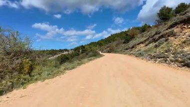 Resimli ve dolambaçlı toprak bir yol zarif bir şekilde dolgun, bulutlu bir gökyüzünün altındaki yemyeşil çimenlikte dolaşır.