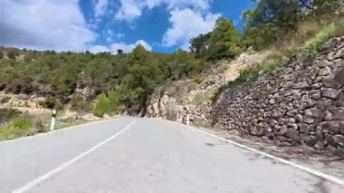 Güzel, dolambaçlı bir yol, parçalı bulutlu bir gökyüzünün altında yeşil ve kayalık duvarlarla çevrilidir.