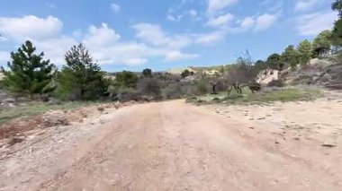 Sakin bir toprak yol, berrak mavi gökyüzü altında canlı yeşillikler ve çarpıcı doğal güzellikler arasında zarif bir şekilde esiyor.