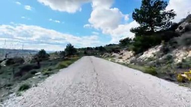 Güzel bir çakıl yolu bulutlarla dolu mavi bir gökyüzünün altında, pitoresk manzaralar arasında yol alır.