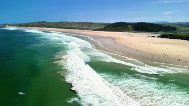 Dalgaların açık gökyüzünün altındaki yumuşak kumlu kıyılara çarptığı nefes kesici bir sahilin geniş bir hava manzarası.