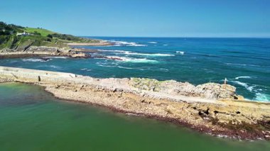 Kayalık kıyıları, berrak suları ve parlak mavi gökyüzünün altında hafif dalgaları olan çarpıcı bir kıyı manzarası.