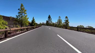 Parlak yeşillik ve açık mavi gökyüzü ile çevrili dolambaçlı bir yolun nefes kesici ve güzel manzarası.