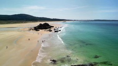 Kristal berraklığında turkuaz su ve manzaralı kayalık oluşumlarla sakin bir plajın nefes kesici ve çarpıcı bir görüntüsü.