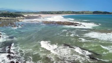Güzel bir kayalık sahil şeridinin ve berrak mavi gökyüzünün altındaki sakin plajın nefes kesici insansız hava aracı görüntüleri..
