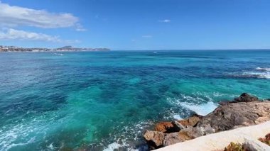 Parlak mavi okyanusun berrak, güneşli bir gökyüzünün altında kayalık kıyı şeridi ile buluşmasının nefes kesici, nefes kesici bir görüntüsü.