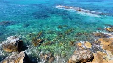 Kristal berraklığında, canlı mercan resifleri ve kıyı kayalarını gösteren okyanusun nefes kesici manzarasını deneyimleyin.