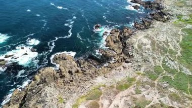 Okyanus kıyısındaki engebeli bir kıyı şeridine çarpan çarpıcı dalgaların nefes kesici hava görüntülerini tecrübe edin.