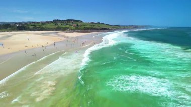 Sörfçülerle, güneşlenenlerle ve pırıl pırıl berrak mavi sularla dolu canlı bir plajı gösteren nefes kesici bir hava manzarası.