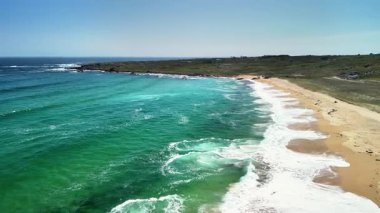 Nefes kesici bir hava manzarası, turkuaz suların ve parıldayan altın kumların yer aldığı huzurlu bir sahil sahnesini yakalıyor.