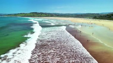 Yuvarlanan dalgalar ve güneş banyosuyla dolu canlı bir sahilin havadan görünüşü, rahatlama ve eğlence için mükemmel bir gün.