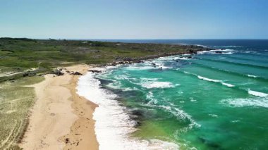 Hava görüntülerinde, gök mavisi, berrak suları ve zahmetsizce süzülen nazik dalgalarıyla nefes kesici bir sahil görülüyor.