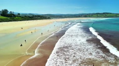 Güzel güneşli bir sahil, rahatlatıcı dalgaları olan, insanların dinlendiği ve nefes kesici kıyı manzaralarının tadını çıkardığı.