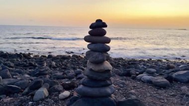 Huzurlu ve sakin bir taş yığını kumlu sahilde canlı bir günbatımına karşı güzelce yerleştirilmiş.