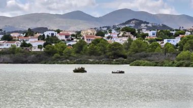 Huzurlu bir göl hayal edin, yemyeşil ağaçlar, arka planda görkemli dağlar, ve yakınlarda büyüleyici evler.