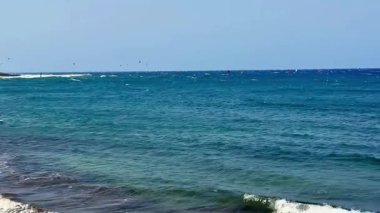 Sakin bir sahil manzarası güzel mavi bir okyanus, nazik dalgalar ve saf neşe için heyecan verici rüzgar sörfü gösteriyor.