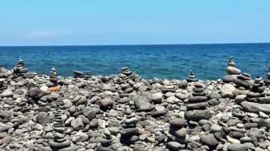 Huzurlu ve huzurlu bir sahil sahnesi. Dengeli taş yığınları çarpıcı mavi bir okyanus zeminine karşı.