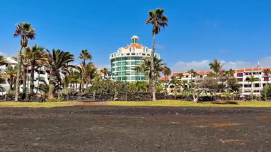 Benzersiz bir volkanik manzaradaki yemyeşil palmiye ağaçları arasında çarpıcı bir tropikal tatil köyünün panoramik manzarasının tadını çıkarın.