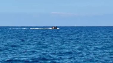 Hızlı bir motorlu tekne parlak ve berrak bir gökyüzünün altında canlı mavi okyanus dalgaları üzerinde hızla süzülüyor.