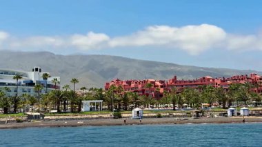 Palmiye ağaçları, güzel bir sahil ve görkemli dağlarla lüks bir sahil manzarası.