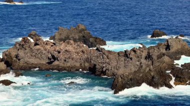 Çarpışan dalgaları ve canlı mavi okyanusuyla güzel, kayalık bir sahil şeridi büyüleyici bir manzara yaratır.