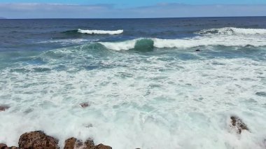 Sakin, sakin bir sahil manzarasında dalgaların engebeli kayalara çarptığı nefes kesici okyanus manzarasının tadını çıkarın.