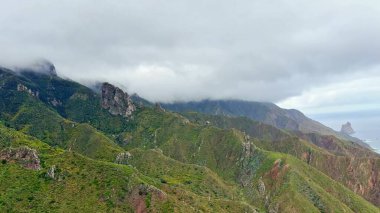 İnce bulutlarla kaplanmış görkemli dağların nefes kesici manzarası zengin, canlı yeşillikler sergiliyor.