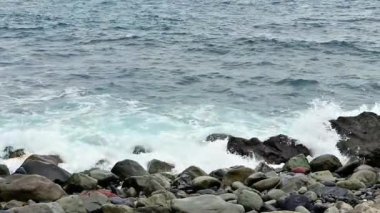 Dalgaların engebeli kayalara çarpıp sahilin güzelliğini gösteren manzaralı bir manzara.