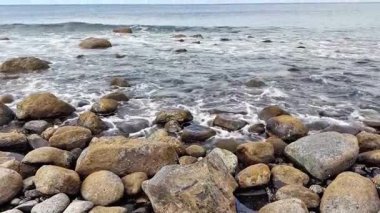 Deniz kenarındaki engebeli kayaların sakin manzarasının tadını çıkarıyorum. Yumuşak dalgalar kıyıya vuruyor, huzur ve güzellik yaratıyor.