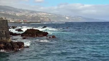Berrak bir gökyüzünün altındaki engebeli kayalara çarpan dalgaların çarpıcı kıyı manzarası.