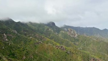 Puslu bulutlarla kaplanmış yemyeşil bir dağ silsilesinin nefes kesici manzarasını tecrübe edin.