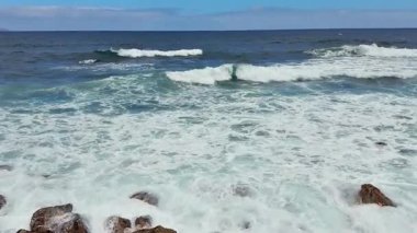 Sakin, sakin bir sahil manzarasında dalgaların engebeli kayalara çarptığı nefes kesici okyanus manzarasının tadını çıkarın.