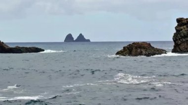 İkiz kaya oluşumları okyanus dalgalarından çarpıcı bir şekilde yükselir, bu sakin kıyı sahnesinde güzel bir şekilde yakalanır.