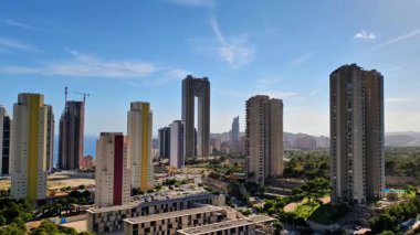 Göz kamaştırıcı bir ufuk çizgisi açık mavi gökyüzünün altında yemyeşil ve yüksek binalar sergiliyor.