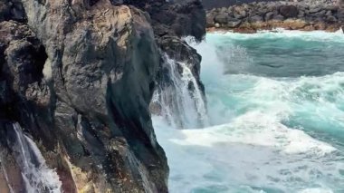 Okyanus dalgalarının nefes kesici ve çarpıcı görüntüsü dinamik bir kıyı sahnesinde engebeli kayalara çarpıyor.