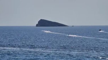 Sersemletici bir deniz manzarası, derin mavi bir okyanusta sakin sularda süzülen tekneleriyle resim gibi bir adaya ev sahipliği yapar.