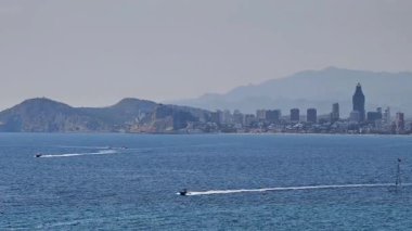 Dalgalı bir sahil şehrinin büyüleyici manzarasının tadını çıkarın. Gemiler görkemli dağ arkaplanlarına karşı suyun üzerinde süzülüyor.