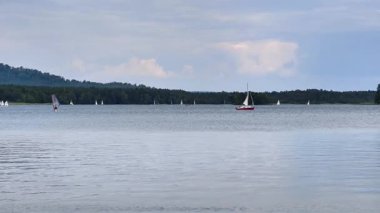 Renkli yelkenlileri gösteren manzaralı bir manzara bulutlu bir arkaplan altında sakin bir gölde süzülüyor.
