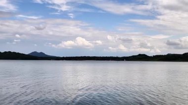 Yumuşak dalgaların, arka planda uzak tepelerin ve yukarıda dinamik bulutların olduğu sakin ve sakin bir göl.