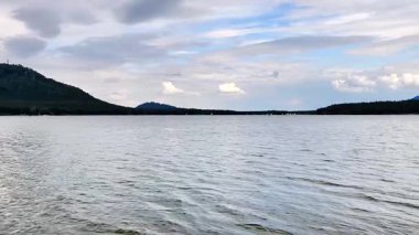 Sakin ve sakin bir göl sahnesi. Huzurlu bir gökyüzünün altında yükselen uzak tepeler gibi hafif dalgalar.