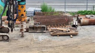 Çeşitli sondaj ekipmanları ve çok çeşitli inşaat malzemeleriyle dolu hareketli bir inşaat alanı.