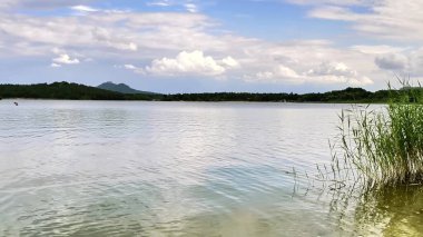 Sakin suları, yumuşak dalgaları ve mavi gökyüzünün altındaki uzak dağları barındıran sakin bir göl manzarası..