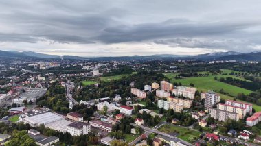 Göz kamaştırıcı bir hava görüntüsü, yemyeşil manzaralar ve bulutlu gökyüzünün ortasında yer alan modern bir kentsel alanı parlak bir şekilde yakalıyor.