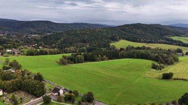 Bulutlu gökyüzünün altındaki canlı yeşil tarlaların ve tepelerin havadan görünüşü sanatın güzelliğini gözler önüne seriyor.