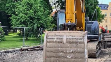 Bir kazıcı aktif olarak ağaçların arasında çalışıyor, önemli bir park alanı inşaatına zemin hazırlıyor.