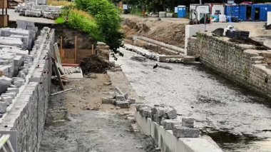 Su yolu boyunca bir inşaat alanının manzaralı görüntüsü, devam eden ilerlemeyi ve çeşitli materyalleri vurguluyor