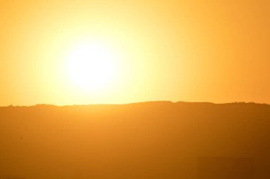 Göz kamaştırıcı bir gün batımı şehri, altın rengi gökyüzü uzak tepelerin üzerine sıcak renkler döküyor. Siluetli binalar çarpıcı bir kontrast oluştururken kuşlar ufuk çizgisinin üzerinde süzülüyor. Bu huzurlu şehir manzarası, Alacakaranlık 'ın mimari cazibesini yansıtıyor.