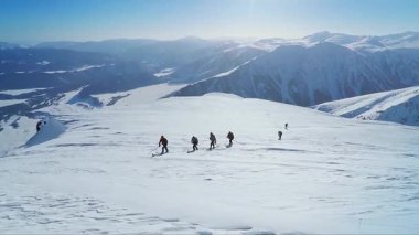Karlı bir dağa tırmanan kayak giyen bir grup insanın videosu.