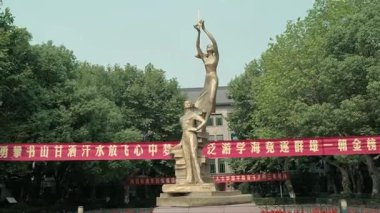 Bir Genç Erkek ve Kız heykeli, 124ncü bina videosu insanları sıkı çalışmaya teşvik eden kırmızı pankart.